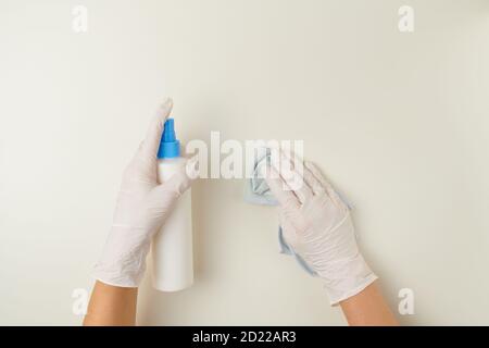 Obere Ansicht der Hände von Frauen in weißen Gummihandschuhen, die die Tischoberfläche mit Desinfektionsmittel und Reinigungstuch desinfizieren. Stockfoto