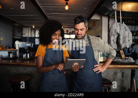 Afroamerikanische Frau und männliche Besitzer lächeln beim Ablesen von digitalen Tablet im Café. Stockfoto