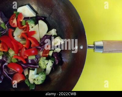 Nahaufnahme von veganen Rührbraten Mahlzeit Bio frischen Garten Gemüse von Tomaten, Brokkoli, Pfeffer, Kohl gekochtes Kokosöl in Metall Wok gelben Hintergrund Stockfoto