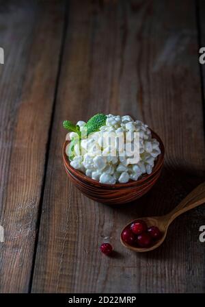 Granulierter Hüttenkäse in einer Keramikschale auf einem Holzhintergrund. Gesunde Ernährung Konzept. Stockfoto