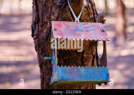 Ein Holzdosierer mit Flecken von mehrfarbiger Farbe hängt an Ein Baum im Wald Stockfoto