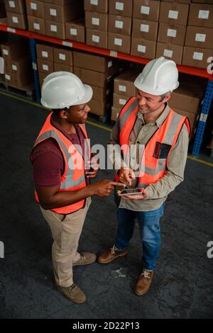 Zwei Geschäftsleute tragen Hardhats tun Forschung für die Verarbeitung von Lieferungen Halten des digitalen Tablets im Lager Stockfoto