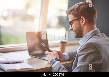 Seitenansicht eines jungen Geschäftsmannes oder männlichen Freiberuflers mit Sein Smartphone während der Arbeit online Remote im Café Stockfoto