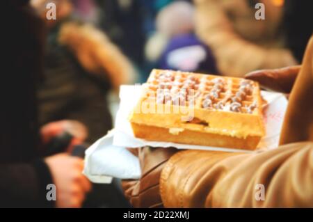 Verschwommenes Foto eines Mannes, der vorsichtig eine belgische Waffel in der Menge des Weihnachtsmarktes trägt. Paris (Frankreich). Stockfoto