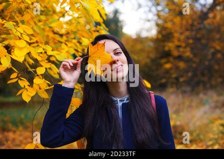 Schöne lächelnde Brünette Abdeckung ein Auge mit gelben Ahornblatt. Genießen Sie den indischen Sommer. Stockfoto