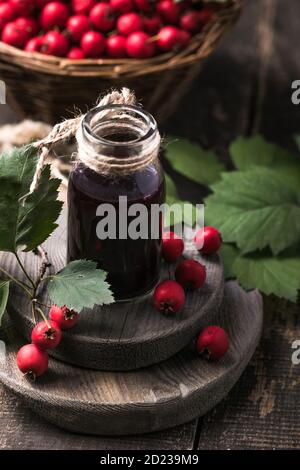 Weißdornbeeren Tinktur oder Infusionsflasche und Korb mit Dornenäpfeln auf Holzbrett. Kräutermedizin. Stockfoto