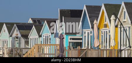 Reihe Von Bunten Hölzernen Strandhütten Mit Sonnenschirmen. Aufgenommen in Mudeford Sandspit UK Stockfoto