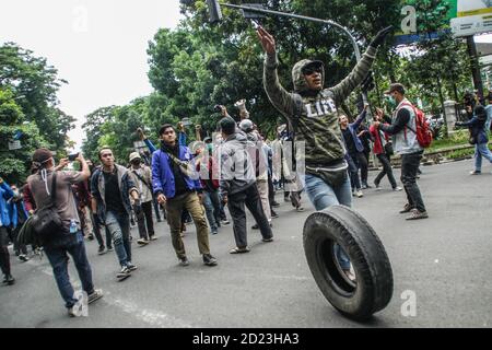 Bandung, Indonesien. Oktober 2020. Ein Protestler macht während des Protestes Gesten, während er einen Autoreifen vor das Parlamentsbüro rollt. Studenten protestierten gegen den Omnibus-Gesetzentwurf der Regierung zur Schaffung von Arbeitsplätzen, der das Wirtschaftswachstum ankurbeln und Arbeitsplätze schaffen sollte, was ihrer Meinung nach die Arbeitnehmer ihrer Rechte berauben und die Umwelt in Indonesien untergraben würde. Kredit: SOPA Images Limited/Alamy Live Nachrichten Stockfoto