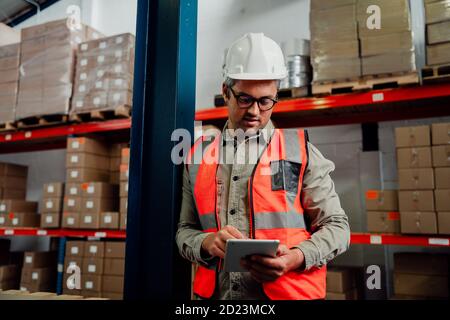 Männlicher Arbeiter, der im Stehen auf einem digitalen Tablet surft und eine Brille trägt Im Werk Stockfoto