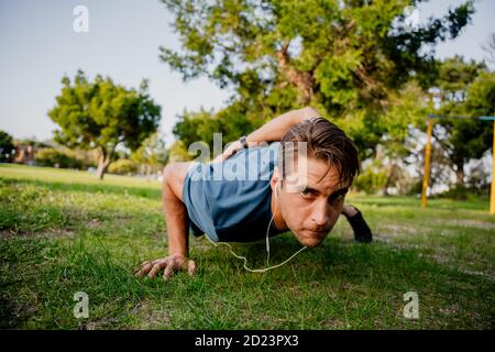 Schöner junger Athlet, der im Freien ein Hand-Push-up durchführt park suchen konzentriert mit Ohrhörern für Musik Stockfoto