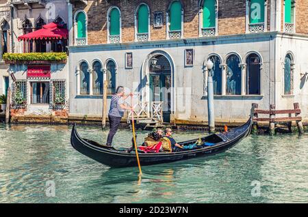 Venedig, Italien, 13. September 2019: Gondoliere und Touristen auf Gondel traditionelle Boot Segeln auf dem Wasser des Canal Grande Wasserstraße mit venezianischer Architektur typischen bunten Gebäuden Hintergrund Stockfoto