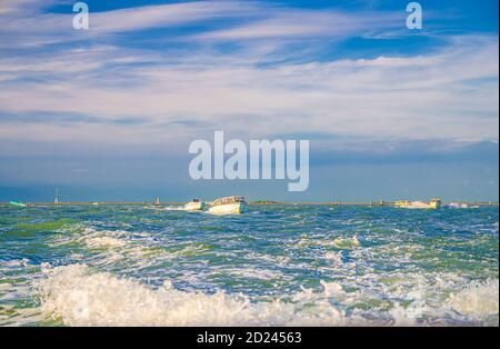 Segelboote, die auf dem Wasser der venezianischen Lagune zwischen Holzmasten in der Nähe der Stadtküste von Venedig, Insel am Horizont, Region Venetien, Norditalien segeln Stockfoto