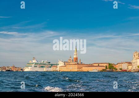 Weißes großes Kreuzfahrtschiff, das im Flusslauf des San Marco-Beckens des venezianischen Lagunenwassers hinter der Insel San Giorgio Maggiore segelt, mit Campanile San Giorgio, Region Venetien, Norditalien. Kreuzfahrtschiff in Venedig Stockfoto