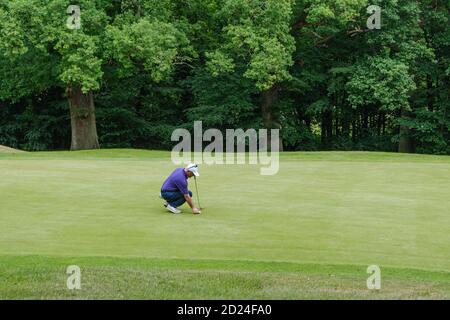 Ein männlicher Golfer hockt sich, um seinen Ball für den Schuss auf das Grün im Pinner Hill Golf Club, Pinner, Middlesex. Stockfoto