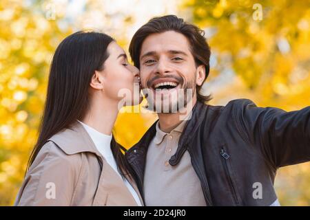 Junge Frau küsst ihren Mann, während sie Selfie nimmt Stockfoto