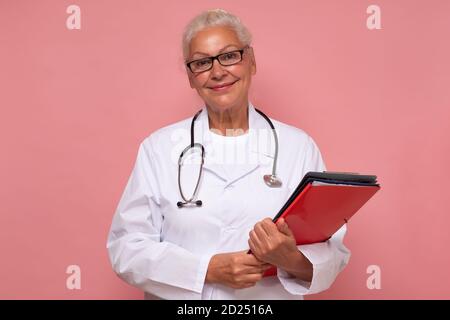 Ältere Ärztin mit Ordnern, die mit einem Lächeln auf die Kamera schauen. Stockfoto