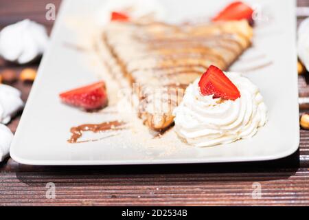 Köstlicher Pfannkuchen mit Erdbeere und Sahne auf dem Holzhintergrund Stockfoto