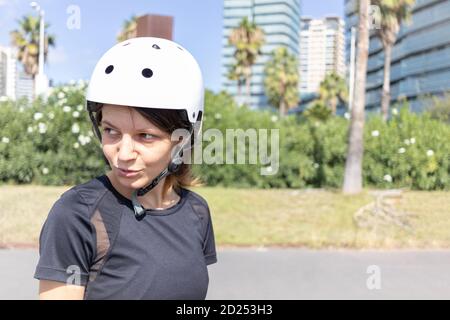 Junge Roller Skater kaukasische Frau in den weißen Helm und schwarze sportliche Kleidung an einem sonnigen Tag im Skatepark, städtische Umwelt Stockfoto