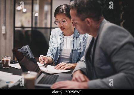 Zwei verschiedene Geschäftsleute, die bei der Arbeit zusammen über Schreibarbeit gehen Ein Tisch im Büro Stockfoto