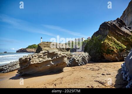 Riesige Felsbrocken am Sandstrand Miramar Plage mit Blick auf den weißen Leuchtturm - Phare de Biarritz an der Pointe Saint-Martin. Bucht von Biskaya, Atlanti Stockfoto