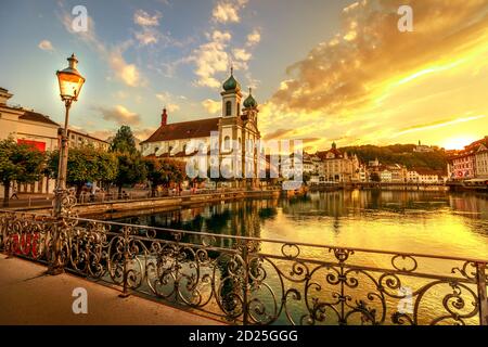 Farbenprächtiger Sonnenuntergang in Luzern Stadt am Vierwaldstättersee in der Schweiz. Am Reuss spiegelt sich die Jesuitenkirche oder die Kirche St. Franz Xaver. Fußgänger Stockfoto