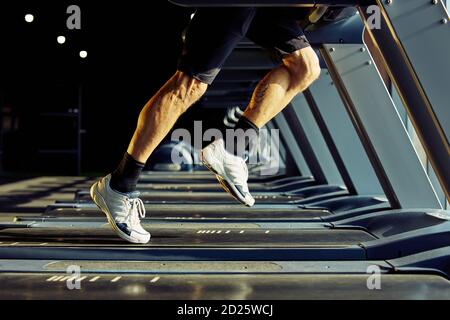 Kurze Aufnahme eines sportlichen Mannes in Sportbekleidung, der auf einem Laufband in einem Fitnessstudio läuft, konzentrieren Sie sich auf die Beine Stockfoto