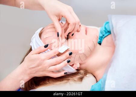 Kinesiotaping. Junge Frau liegt mit Klebeband auf ihrem Gesicht. Physiotherapie und Kosmetologie Verfahren. Methode der nicht-chirurgischen Hautverjüngung. Gesichtshaut Stockfoto