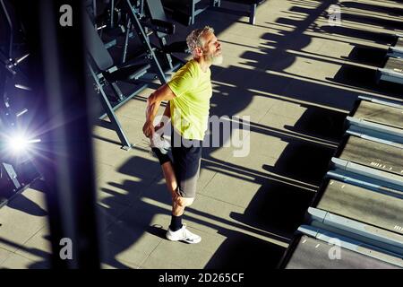 Ganzkörperaufnahme eines reifen Sportlers, der Stretching-Übungen macht und sich vor dem Training im Fitnessstudio aufwärmt Stockfoto