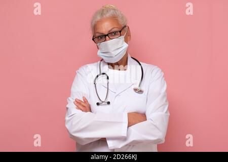 Ältere Frau mit Stethoskop trägt Maske Arzt Studio isoliert auf Rosa Wand Stockfoto