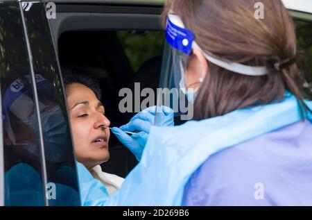 Asiatische Frau in einem Auto mit einem Coronavirus Nasenabstrich Test mit einer Krankenschwester in PSA-Ausrüstung. England, Großbritannien Stockfoto