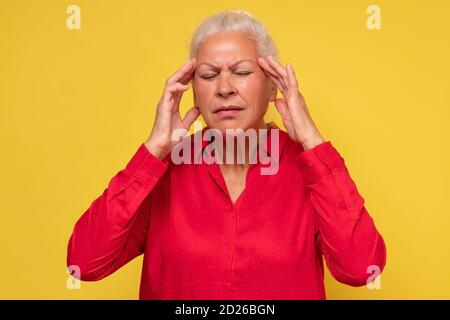 Ältere Frau, die ihre Hände an ihre Schläfen hält und schreckliche Kopfschmerzen hat. Stockfoto