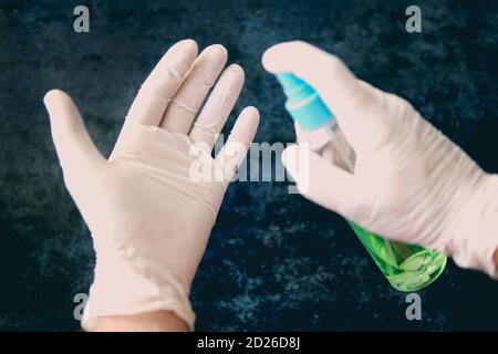 Mann Hand in Gummi-OP-Handschuhe hält antiseptische Hand Desinfektionsmittel auf dunklem Hintergrund. Alkohol Desinfektionsmittel Handhygiene Corona Virenschutz Stockfoto