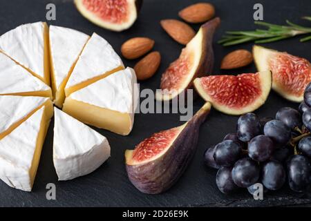 Camembert Käse mit Feigen und Trauben auf schwarzem Schiefer Hintergrund. Vorspeise Käseplatte Stockfoto