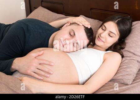 Liebende schwangere Paar Umarmungen auf dem Bett am Morgen. Stockfoto