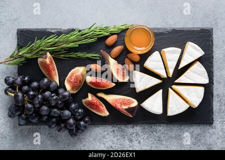 Camembert Käseplatte mit Feigen, Trauben, Honig und Nüssen auf schwarzem Schiefer serviert. Draufsicht Stockfoto