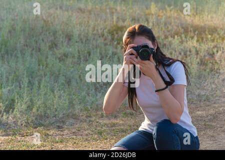 Junge Fotografin schaut in ihre Spiegelreflexkamera und macht Fotos. Eine schöne Brünette in einem weißen T-Shirt und Jeans setzte sich, ein Profi Stockfoto