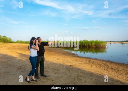 Mann und Frau Fotografen am Flussufer an einem Sommertag. Junge Brünette macht Bilder von der Natur. Stockfoto