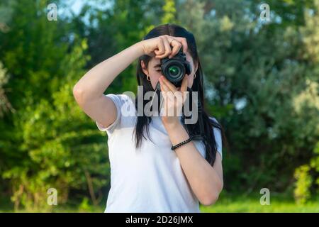 Eine junge Frau schaut in die Linse ihrer Kamera. Der Fotograf nimmt Bilder an einem Sommertag auf, mit selektivem Fokus. Stockfoto