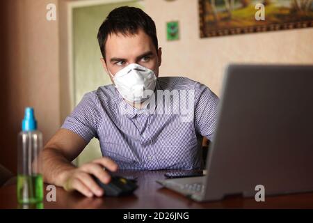 Junger Mann trägt medizinische Gesichtsmaske bei der Arbeit von zu Hause aus Büro wegen Corona Virus Ausbruch mit Laptop auf Holztisch, Remote-Arbeit vor Hintergrund Stockfoto