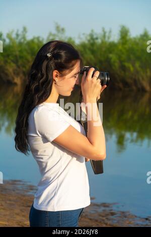 Schöne junge Frau fotografiert die Landschaft an einem Sommertag in der Nähe des Flusses. Schönes Bokeh, selektiver Fokus. Stockfoto