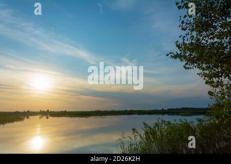 Sonnenuntergang über dem Fluss im Sommer. Die Sonne geht am Horizont unter. Flusslandschaft im Sommer, Nebelblick. Stockfoto