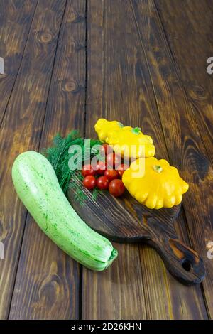 Buntes Gemüse auf dunklem Holztisch. Gelb, grün und rot. Kirschtomate, Zucchini, Mini-Patty Pfanne Squashes, Dill. Helle Ernte der vegeta Stockfoto