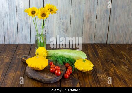 Buntes Gemüse auf dunklem Holztisch. Vase mit gelben Blüten. Gelb, grün und rot. Kirschtomate, Zucchini, Mini-Patty Pfanne Squashes Stockfoto