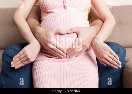 Schwangerschaft, Erwartung eines Kindes. Zukünftige Eltern mit Händen in Form von Herz. Der Mann legte seine Hand auf den Bauch der Frau. Stockfoto