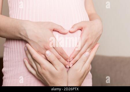 Schwangerschaft, Erwartung eines Kindes. Zukünftige Eltern mit Händen in Form von Herz. Der Mann legte seine Hand auf den Bauch der Frau. Stockfoto