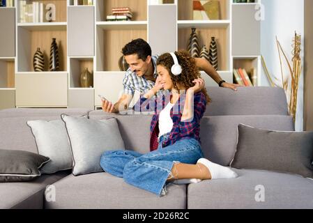 Glückliches junges Paar entspannt die Wahl Musik zusammen auf einem Handy Telefon im Wohnzimmer und genießen eine gute Zeit Stockfoto