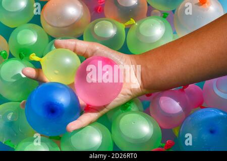 Person, die eine Handvoll farbenfroher Wasserbomben in Latex hält Oder Gummiballons im Vollformat aus nächster Nähe Anzeigen Stockfoto