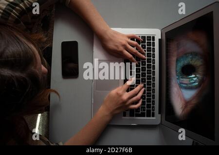 Junge Frau mit Computer zum Einkaufen oder Arbeit infiziert mit Spyware oder Malwear, große Augen beobachten vom Bildschirm, Konzept Stockfoto