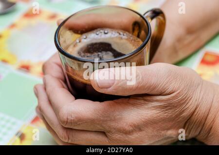 Eine ältere Frau hält eine schwarze Tasse heißen Kaffees in ihren Händen. Stockfoto