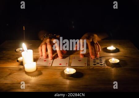 Hände eines Wahrsager und Karten auf dem Tisch, um brennende Kerzen im Dunkeln auf einem Holztisch. Konzept der Weissagung, Magie Stockfoto